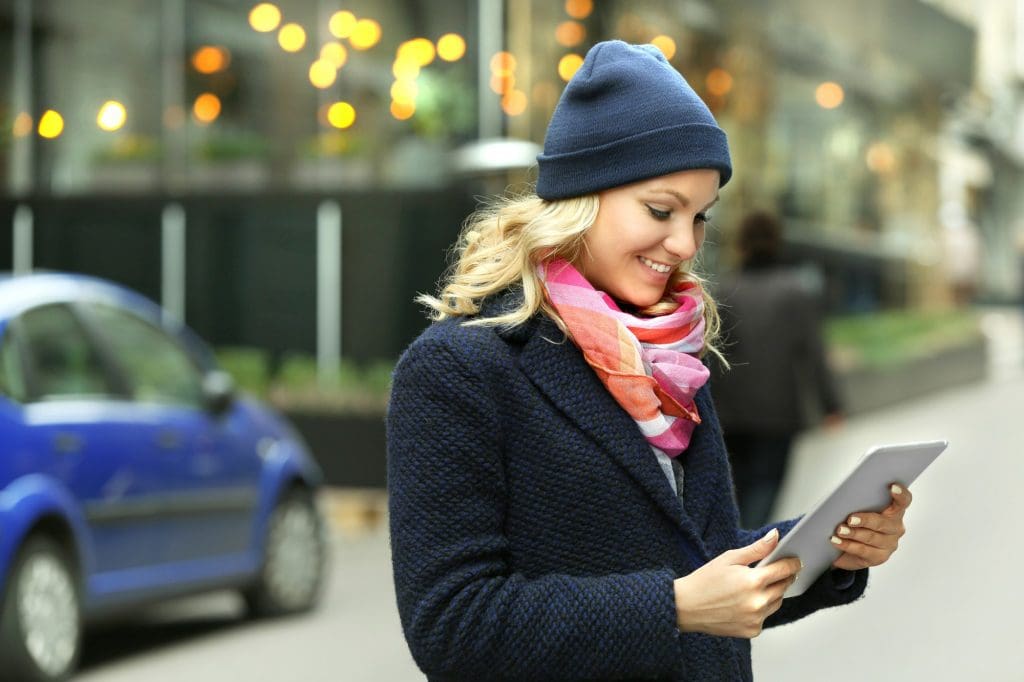 woman standing on the side of a street holding a tablet, possibly researching EV insurance UK