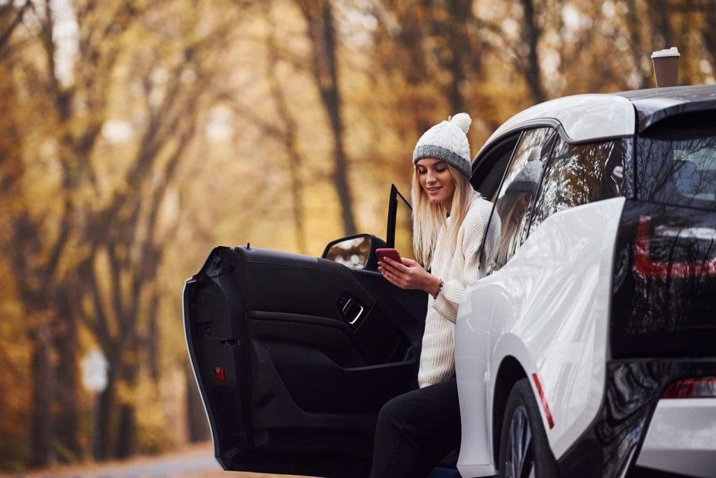 woman sitting on the back of a white car, highlighting the importance of EV range in cold weather