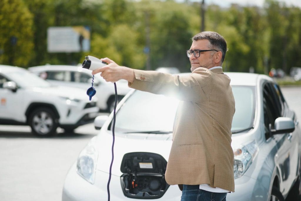 man in a parking lot holding a car charger for EV charging for company car drivers