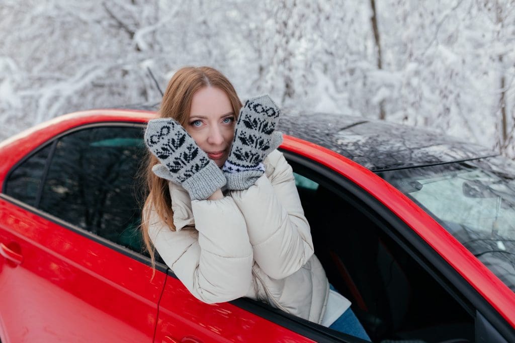 woman sitting in a red car in the snow with EV winter accessories UK