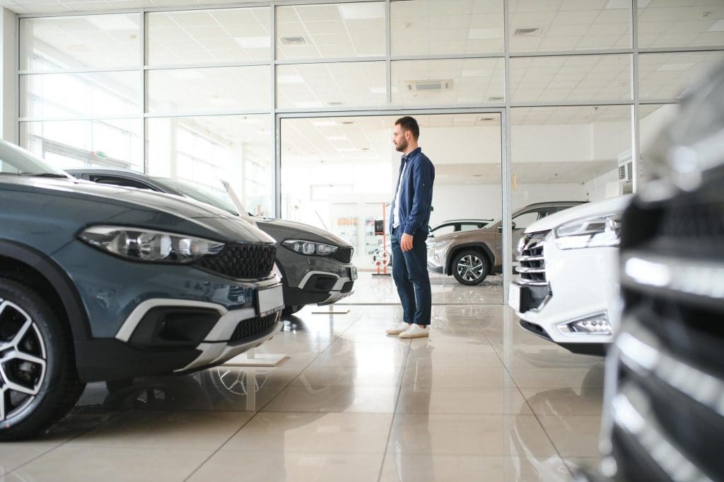 man standing next to two cars in a showroom