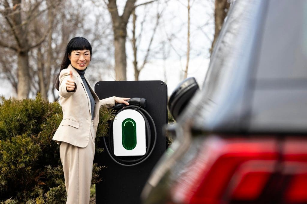 woman standing next to a car giving a thumbs up, showcasing positive ev charging etiquette in the UK