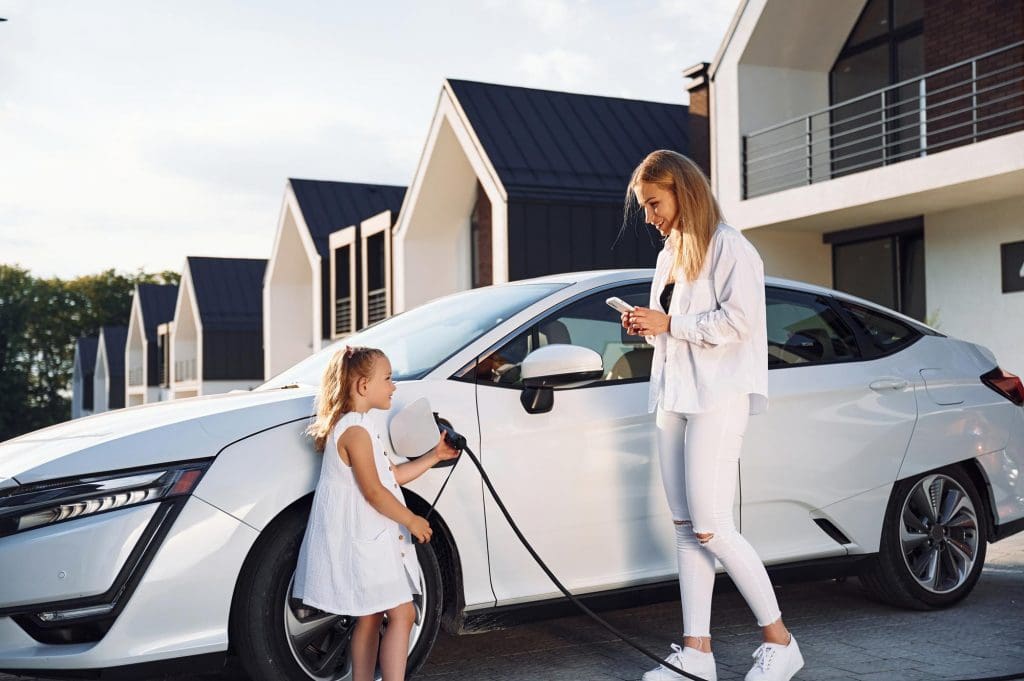 woman and a little girl are charging an electric vehicle while considering ev insurance uk 2025