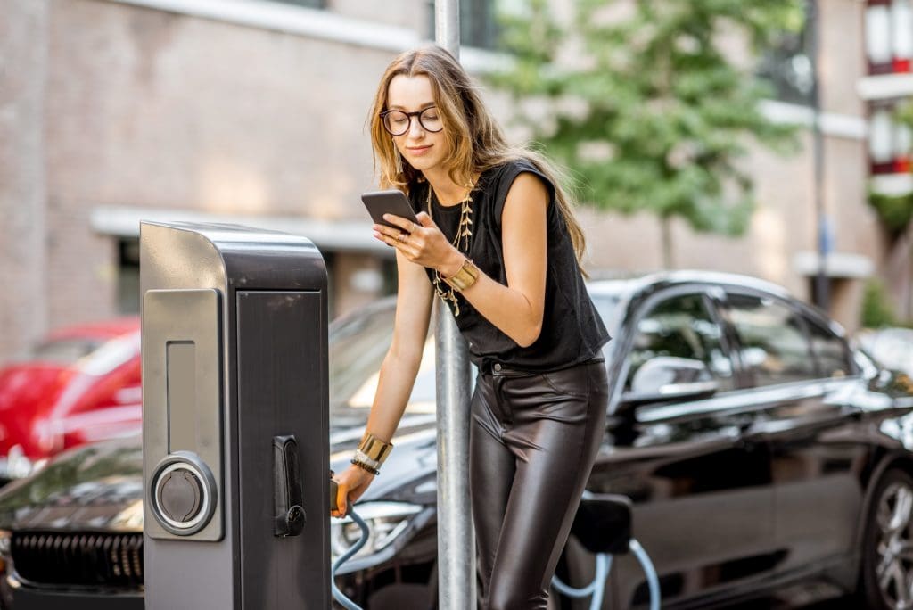 woman in a black top is using a cell phone, possibly checking Instant EV charging receipts UK