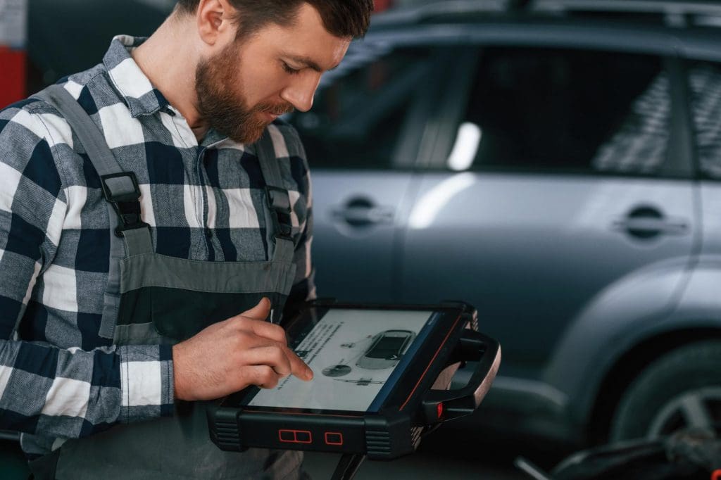 man standing in front of a car holding a tablet, possibly discussing ev maintenance myths in the UK