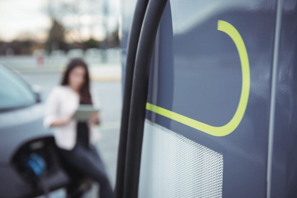 Public EV charger beside an electric car with a driver in the background